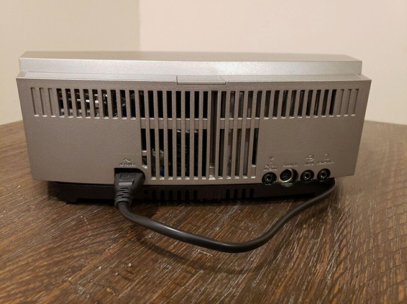 May include: The back of a silver stereo system with a black power cord plugged in. The stereo has a series of vents and several ports on the back.