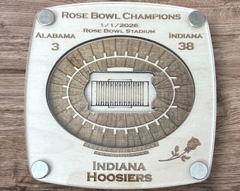 Puede incluir: Un recuerdo de madera de los campeones del Rose Bowl con los Indiana Hoosiers. El diseño incluye el diseño del estadio, los resultados de Alabama (3) e Indiana (38), la fecha 1/1/2026 y un emblema de rosa. La pieza es cuadrada con cuatro imanes plateados.