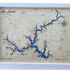 May include: A wooden map of Lake Sinclair in Georgia, USA. The lake is shown in blue, with the surrounding land in a light wood color. The map includes the lake's name, the state, and the country. The map also includes the latitude and longitude of the lake.