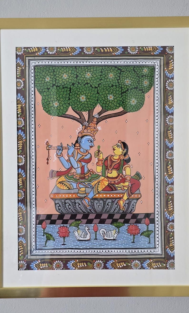 May include: An Indian miniature painting depicting a blue-skinned figure playing a flute, and a woman, seated under a tree. The artwork features intricate details, vibrant colors, and a decorative border, framed in gold.