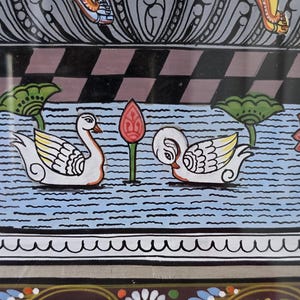 May include: An Indian folk art painting featuring a detailed depiction of swans on a blue water background. The artwork showcases vibrant colors, including white, yellow, red, and blue, with intricate patterns and designs. The painting is framed.