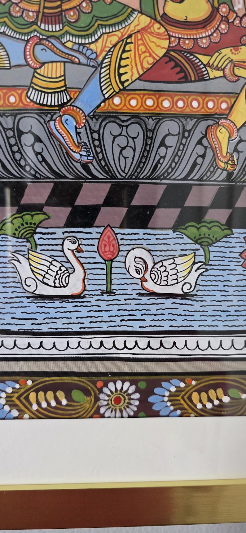May include: An Indian folk art painting featuring a detailed depiction of swans on a blue water background. The artwork showcases vibrant colors, including white, yellow, red, and blue, with intricate patterns and designs. The painting is framed.