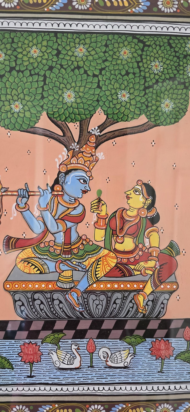 May include: A vibrant Indian painting depicting two figures under a tree. One figure, blue-skinned, plays a flute, while the other, yellow-skinned, holds a leaf. The scene is set against a peach background with a water scene at the bottom.