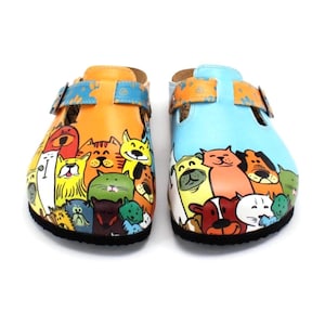 May include: A pair of colorful clogs with a cartoon cat and dog design. One clog is orange with a blue strap, and the other is light blue with an orange strap. The clogs have a black sole.