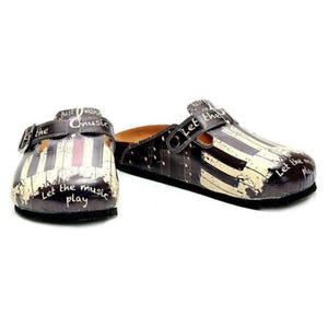 Könnte beinhalten: Braune Clogs mit einem Klaviertasten-Design. Die Clogs haben einen Riemen mit Schnalle und die Worte "Let the music play" und "Just wanna music" sind auf die Clogs gedruckt.