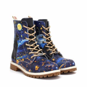 Könnte beinhalten: Paar Kampfstiefel mit Sternennacht-Design. Die Stiefel haben einen dunkelblauen Hintergrund mit Vollmond, einer schwarzen Katzen-Silhouette und goldenen und orangefarbenen Akzenten. Sie haben beige Schnürsenkel und eine braune Sohle.