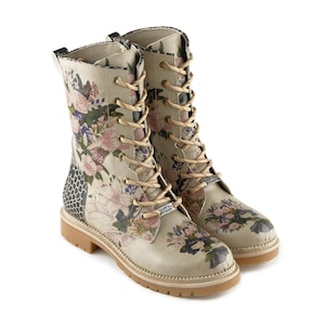 Könnte beinhalten: Beige Combat-Stiefel mit floralem Muster in Rosa, Lila und Weiß. Die Stiefel haben beige Schnürsenkel, eine hellbraune Sohle und ein strukturiertes Seitenteil. Die Stiefel sind ca. 20 cm hoch.