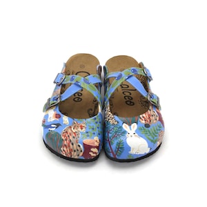 Könnte beinhalten: Blaue Clogs mit einem skurrilen Walddesign, das einen weißen Hasen und einen Fuchs zeigt. Die Clogs haben blaue Riemen mit olivgrünen Details. Der Markenname "alceo" ist auf der Seite aufgedruckt.