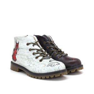 Może przedstawiać: Para botków. Jeden but jest biały z czerwoną grafiką diabła i fakturą przypominającą cegłę. Drugi but jest ciemnobordowy. Oba mają oliwkowozielone sznurowadła i podeszwę z protektorem.