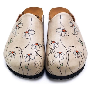 May include: A pair of beige clogs with a black sole, adorned with a hand-painted floral design. The flowers are white with orange centers and are connected by black stems and green leaves. The clogs have a rounded toe and a slip-on design.