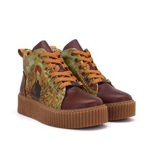 Op de afbeelding: Bruine leren high-top sneakers met een plateauzool. De sneakers hebben een kleurrijk ontwerp met een vrouw in een bosscène op de zijpanelen. De veters zijn oranje en de zolen zijn lichtbruin.