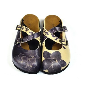 Peut inclure: Une paire de sabots avec des motifs floraux. L'un est violet foncé, l'autre crème. Les deux ont des brides croisées avec des motifs de feuilles et des boucles réglables. Les sabots ont une semelle intérieure en liège. Chaussures élégantes.