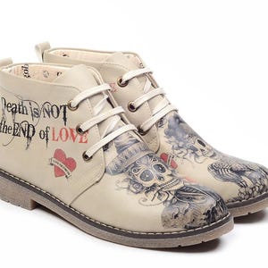 Op de afbeelding: Beige enkellaarsjes met een schedel- en bloementattoo-ontwerp. De laarzen hebben de tekst "Death is NOT the END of LOVE" en een hartafbeelding. Ze hebben witte veters en een lichtbruine zool.
