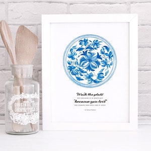 Op de afbeelding: Een wit ingelijst print met een blauw en wit bloemenmotief op een bord. De tekst luidt "Was de plaat niet omdat hij vies is, maar omdat je van de persoon houdt die hem als volgende zal gebruiken."