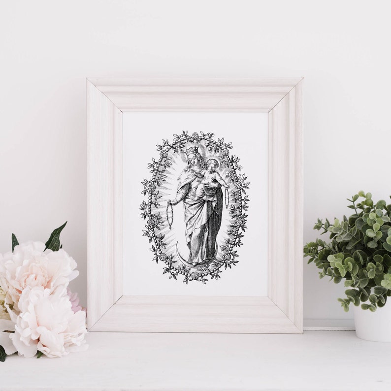 Pu&ograve; includere: Una stampa in bianco e nero incorniciata di una figura religiosa che tiene in braccio un bambino, circondata da un bordo ovale floreale. La stampa &egrave; in una cornice di legno bianca, esposta su una superficie bianca con fiori rosa e una pianta in vaso sullo sfondo.