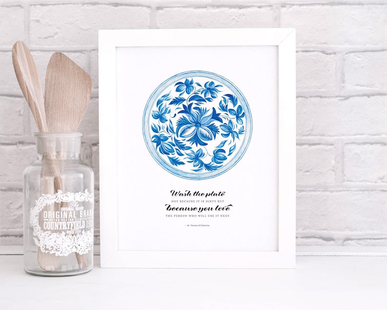 Op de afbeelding: Een wit ingelijst print met een blauw en wit bloemenmotief op een bord. De tekst luidt "Was de plaat niet omdat hij vies is, maar omdat je van de persoon houdt die hem als volgende zal gebruiken."