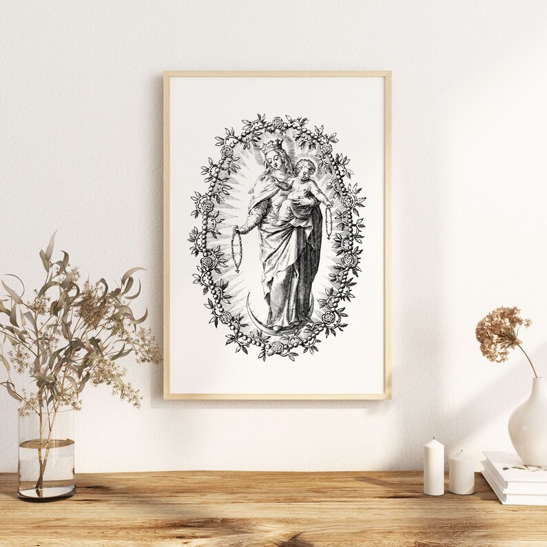 Pu&ograve; includere: Stampa in bianco e nero incorniciata di una figura religiosa che tiene in braccio un bambino, circondata da una ghirlanda floreale. L'opera d'arte &egrave; un'illustrazione dettagliata con un'estetica vintage, su sfondo bianco. La cornice &egrave; di colore legno chiaro.