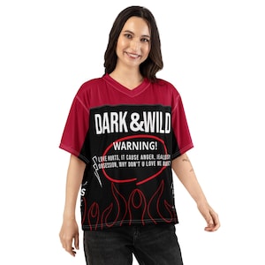May include: A short-sleeve V-neck jersey featuring a maroon upper section and a black lower section. The front displays the white text DARK & WILD, a red oval surrounding the word WARNING!, and the phrase LOVE HURTS, IT CAUSE ANGER, JEALOUSY, OBSESSION, WHY DON'T U LOVE ME BACK? with red flame outlines.