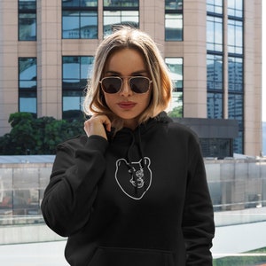 Könnte beinhalten: Schwarzer Hoodie mit einem weißen Umriss eines Bärenkopfes auf der Vorderseite.