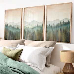May include: Three framed watercolor paintings of a misty forest scene with a soft, muted color palette. The paintings are hung above a bed with a green duvet cover and white and beige pillows.