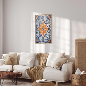 May include: A white sofa with two cushions and a throw blanket in a living room with a framed print of a blue and orange tile design on the wall.