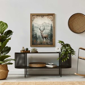May include: A framed print of a watercolor painting depicting a deer standing in a forest with mountains in the background. The print is in a wooden frame with a light brown finish.