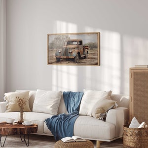 May include: A vintage, rusty blue pickup truck is parked in a field with trees in the background. The truck is framed in a wooden frame and hangs on a white wall in a living room setting.