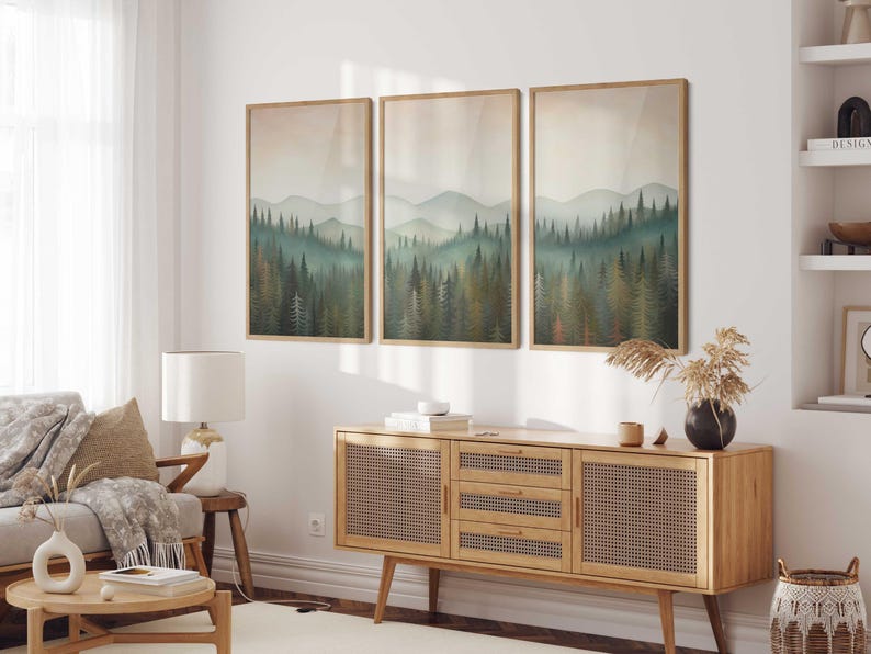 May include: Three framed landscape paintings of a forest with a misty background. The paintings are hung on a white wall above a wooden cabinet with a woven rattan front.