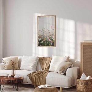 May include: A white couch with brown throw pillows and a brown throw blanket in a living room with a wooden cabinet, a wooden coffee table, and a framed print of a field of wildflowers.