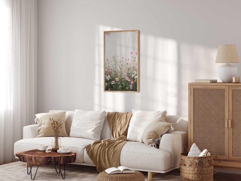 May include: A white couch with brown throw pillows and a brown throw blanket in a living room with a wooden cabinet, a wooden coffee table, and a framed print of a field of wildflowers.
