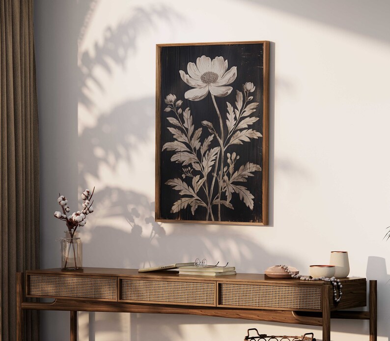 May include: A black and white botanical print of a single flower with leaves on a dark wood background. The print is framed in a dark wood frame.