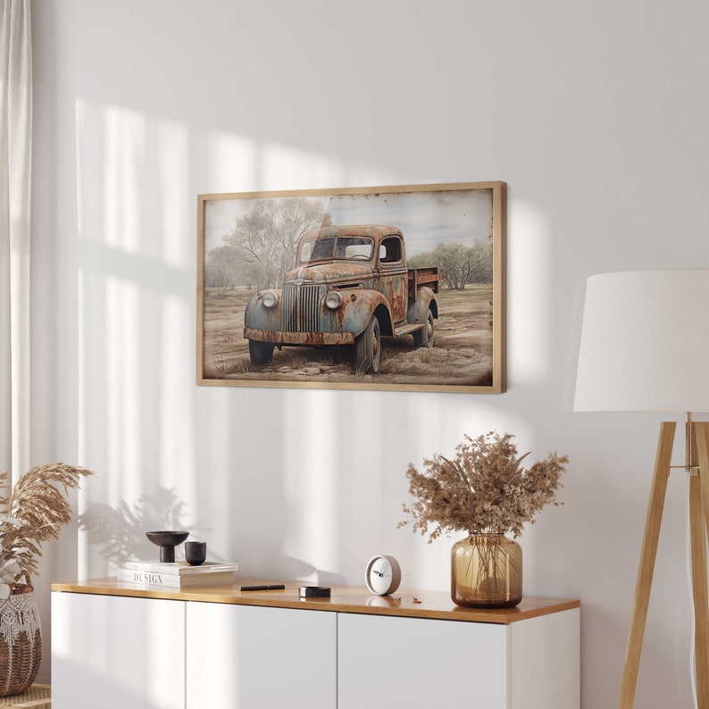May include: A vintage rusty blue pickup truck with a wooden bed sits in a field with trees in the background. The truck is weathered and has a faded blue paint job. The truck is surrounded by dry grass and dirt.
