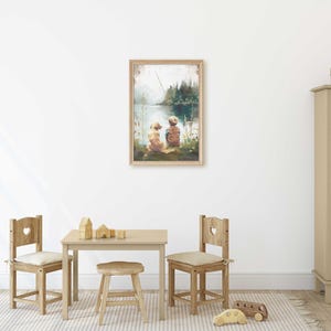 May include: A framed watercolor print depicts two figures sitting by a lake, with a fishing rod in the background. The artwork is displayed on a white wall above a small wooden table and chairs, creating a cozy, inviting atmosphere.