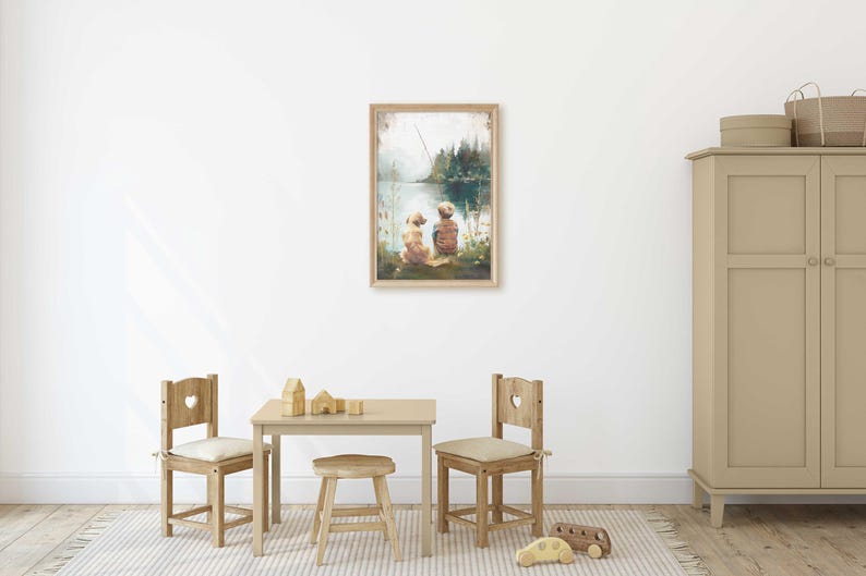 May include: A framed watercolor print depicts two figures sitting by a lake, with a fishing rod in the background. The artwork is displayed on a white wall above a small wooden table and chairs, creating a cozy, inviting atmosphere.