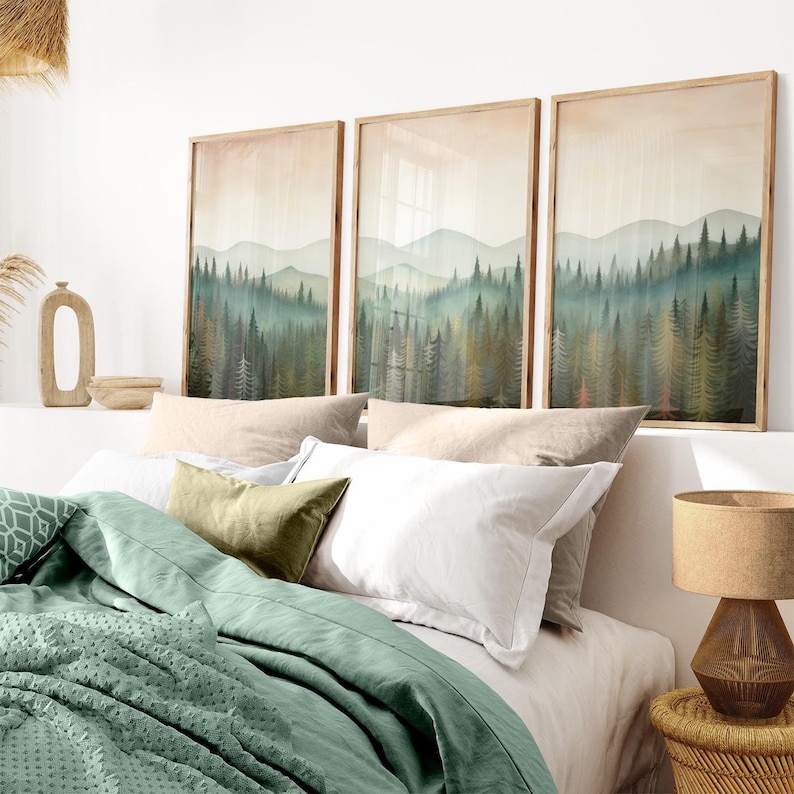 May include: Three framed watercolor paintings of a misty forest scene with a soft, muted color palette. The paintings are hung above a bed with a green duvet cover and white and beige pillows.