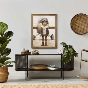 Op de afbeelding: Een ingelijst schilderij van een jong persoon die een bruin leren jack en een vliegeniersbril draagt en voor een klein vliegtuig staat. Het schilderij is geplaatst tegen een witte muur met een zwart metalen plank en een rieten mand op de plank.