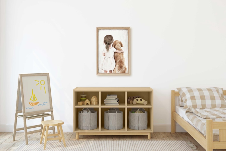 May include: A framed watercolor print depicts a girl in a white dress hugging a golden retriever. The artwork hangs above a wooden storage unit with gray fabric bins. A child's bed with a checkered pillow and a small easel with a drawing are also visible.