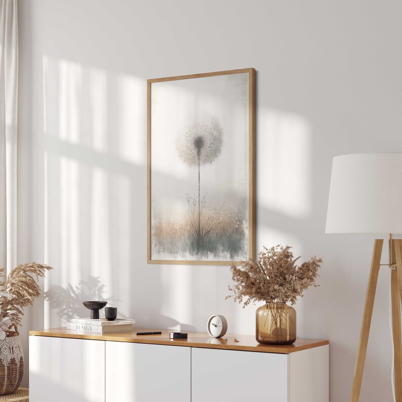 May include: A framed print of a watercolour painting of a dandelion with a soft, muted colour palette. The dandelion is in the centre of the image and is surrounded by a blurred background of grass and foliage.