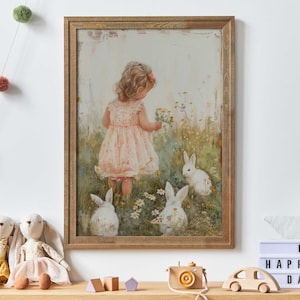 May include: A framed painting depicting a young girl in a pink dress standing in a field of flowers with three white rabbits. The girl is looking down at the rabbits and holding a bouquet of flowers. The painting has a vintage, whimsical feel.