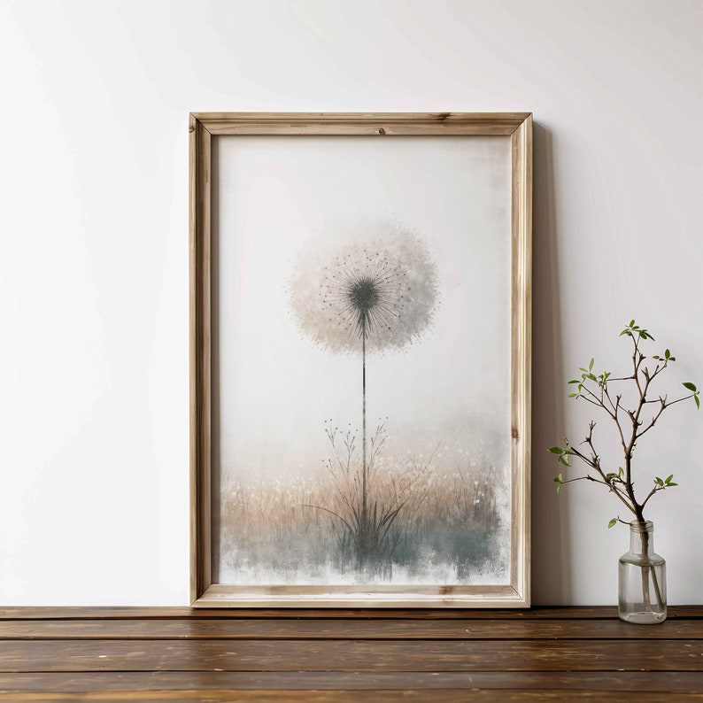 May include: A framed print of a watercolour painting of a dandelion with a soft, muted colour palette. The dandelion is in the centre of the image and is surrounded by a field of grass. The background is a light grey.