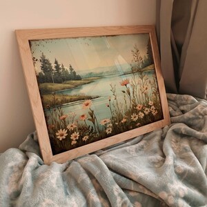 Puede incluir: Una pintura enmarcada que representa una escena de lago con un bosque en el fondo. El lago est&aacute; rodeado de hierba verde y flores silvestres. La pintura tiene un aspecto vintage con una gama de colores azul y verde descoloridos.