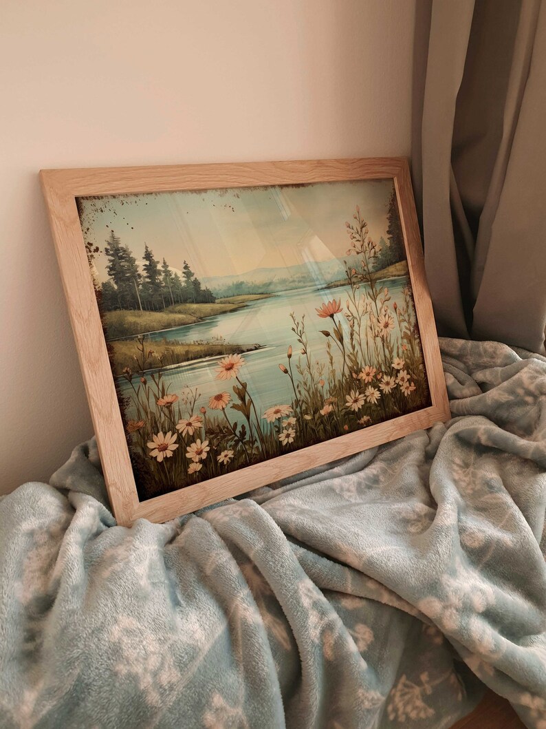 Puede incluir: Una pintura enmarcada que representa una escena de lago con un bosque en el fondo. El lago est&aacute; rodeado de hierba verde y flores silvestres. La pintura tiene un aspecto vintage con una gama de colores azul y verde descoloridos.