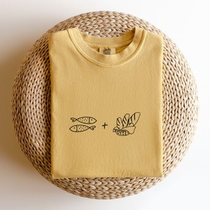 May include: A mustard yellow t-shirt with a graphic of two fish and a loaf of bread. The text "Coffee & Bread" is on the tag.
