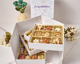 May include: A white gift box with a layered design, filled with assorted Middle Eastern sweets. The box is decorated with a delicate floral pattern and the words "Congratulations" are printed on the top of the box.