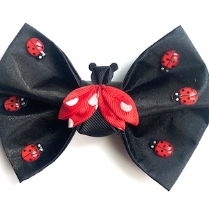 May include: Black satin bow with a red and white polka dot ladybug accent. The bow is decorated with several small red ladybugs.