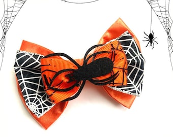 May include: A Halloween-themed bow tie with an orange ribbon base, a black spider, and a white and black spiderweb design. A festive accessory for Halloween.