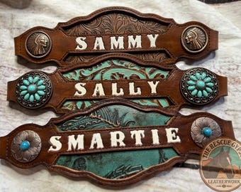 May include: Three personalized leather horse tack nameplates. The top plate reads "SAMMY" in white letters, with a Native American profile on each end. The middle plate reads "SALLY" with turquoise accents. The bottom plate reads "SMARTIE".