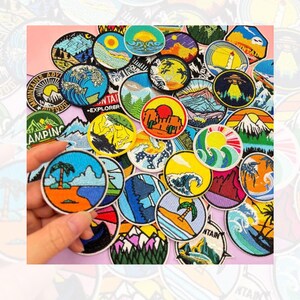 May include: A collection of colorful embroidered iron-on patches featuring various outdoor adventure themes, including mountains, waves, trees, and camping. The patches are circular and have a variety of designs and colors.