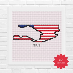 May include: A cross-stitch pattern of the outline of Miami, Florida, in the shape of the American flag. The pattern is in red, white, and blue, with the words "MIAMI" printed below the outline.