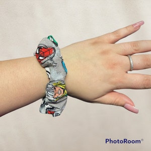 May include: Gray and white scrunchie with a comic book print featuring Spiderman, Thor, and other superheroes.
